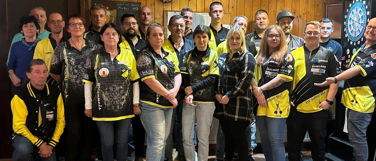 Eine Gruppe von Menschen in gelben und schwarzen Uniformen posiert für ein Foto in einem Raum mit Holzwänden und gefliestem Boden.