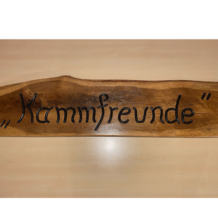 Ein Holzschild mit dem Wort 'Kammfreunde' in Schwarz auf hellbraunem Hintergrund.