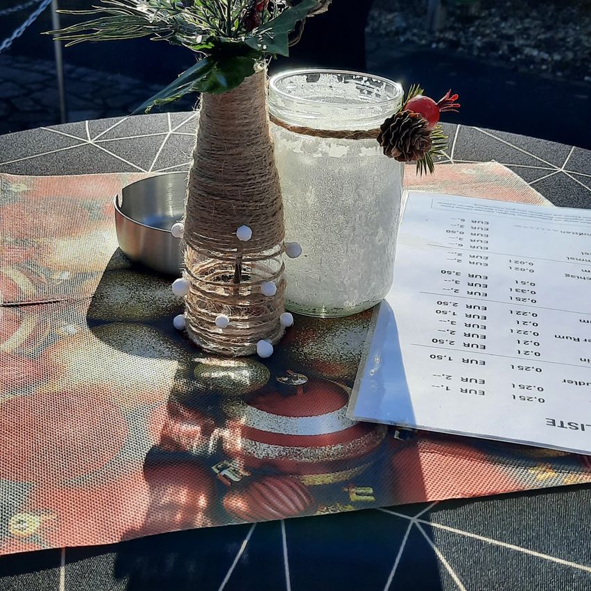 A table setting with a frosted glass, a decorative vase, and a Christmas ornament. A paper with temperatures is placed on the table.