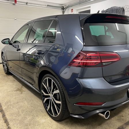 Die Rückseite eines dunkelblauen Volkswagen Golfs ist in einer Garage geparkt, mit roten Rücklichtern, schwarzen Reifen und Felgen sowie einem silbernen Auspuffrohr.