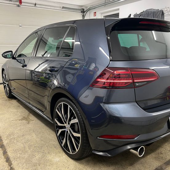 Die Rückseite eines dunkelblauen Volkswagen Golfs ist in einer Garage geparkt, mit roten Rücklichtern, schwarzen Reifen und Felgen sowie einem silbernen Auspuffrohr.