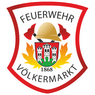Das Emblem der Feuerwehr Volkmarkt, mit einem roten Schild, goldenem Helm und zwei Äxten, einem zentralen Wappen mit einer Burg und dem Jahr 1868 sowie einem Flammendesign.