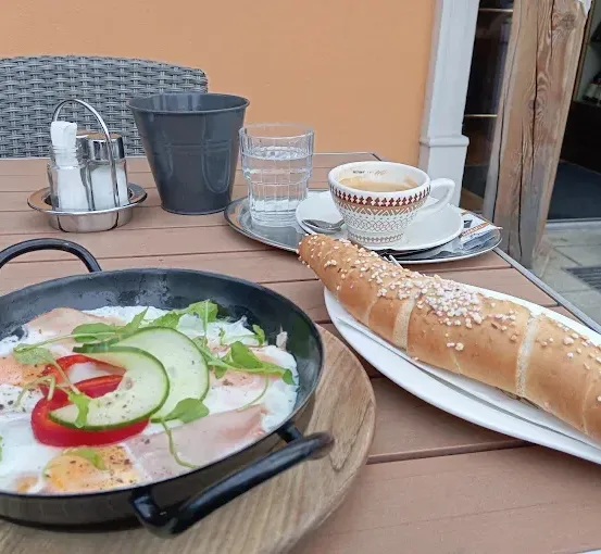 Ein Holztisch hat eine Bratpfanne mit Eiern, Gemüse und Brot. Eine Tasse Kaffee, ein Teller und ein Glas sind in der Nähe.