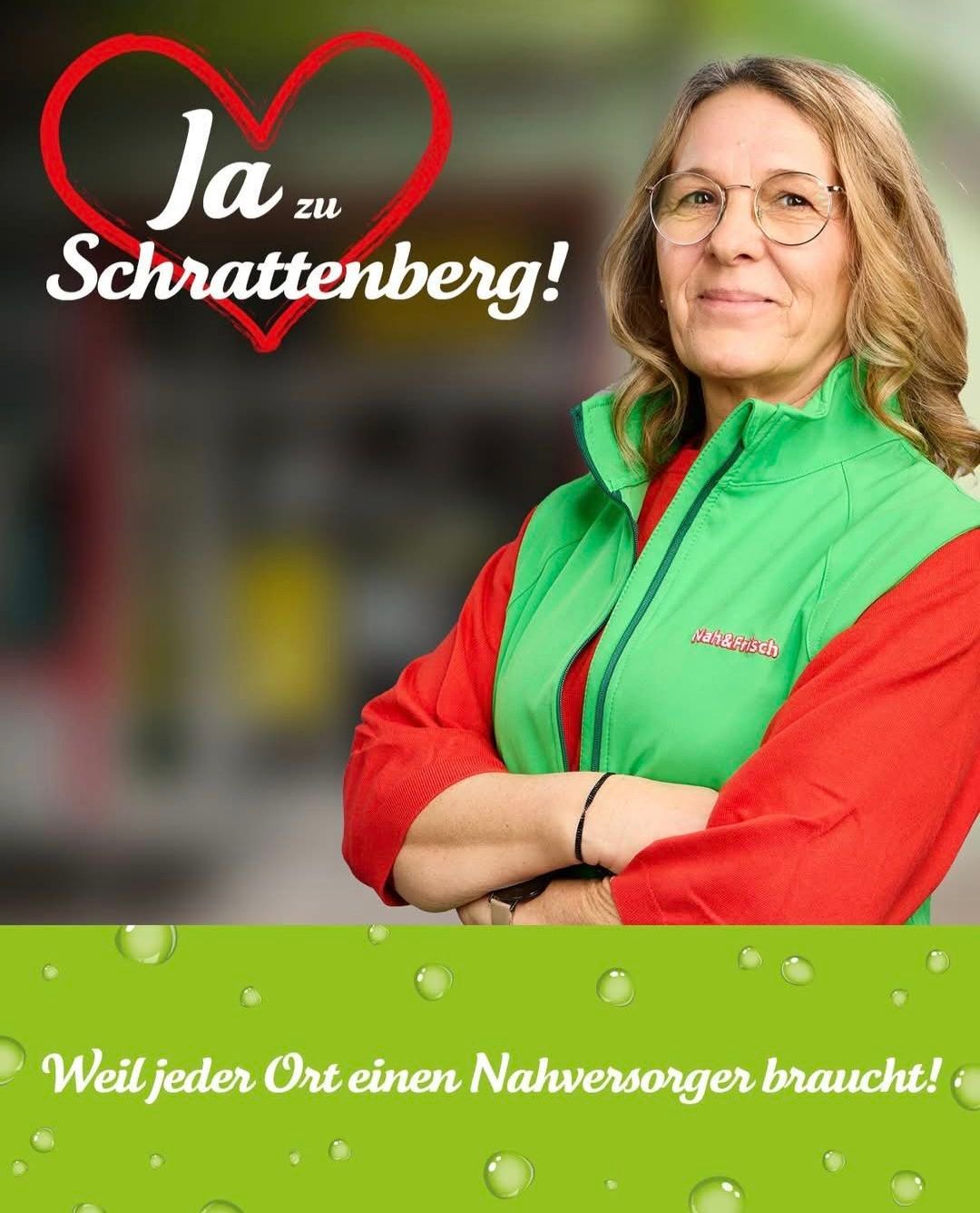 Eine Frau in einer grünen Weste steht mit verschränkten Armen. Der Text 'Ja zu Schattenberg!' ist über ihr in einer roten Herzform angezeigt. Wassertropfen sind unten vorhanden.