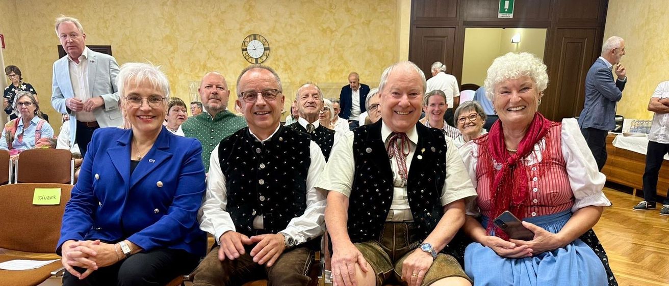 Eine Gruppe älterer Personen in traditioneller Kleidung lächelt und posiert für ein Foto in einem Raum.