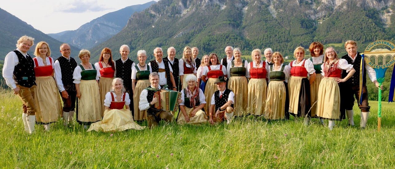 Eine Gruppe von Menschen in traditionellen Kleidern posiert für ein Foto in einer grasigen Wiese mit Bergen im Hintergrund.