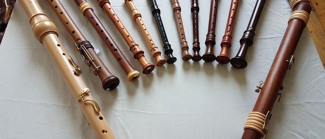 Mehrere hölzerne Blockflöten in verschiedenen Größen und Farben sind auf einem weißen Tuch zu sehen. Die Blockflöten haben unterschiedliche Formen und Größen.