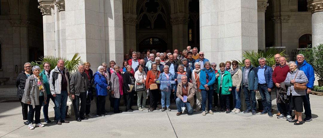Eine große Gruppe von Menschen in warmer Kleidung posiert für ein Foto vor einem historischen Gebäude mit großen Bögen und Säulen.