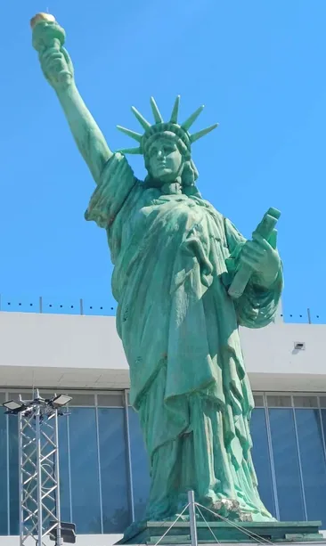 Eine grüne Statue der Freiheitsstatue steht vor einem Gebäude mit blauem Himmel oben.
