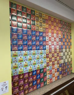 Eine leuchtend gelbe Wand, geschmückt mit einer Vielzahl farbenfroher, rechteckiger Geschenkboxen, die jeweils einzigartig gestaltet und in einem Rastermuster ordentlich angeordnet sind.