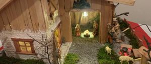Eine kleine hölzerne Krippe mit Figuren von Jesus, Maria und Josef in einer Stallung. Um die Krippe herum befinden sich kleine Figuren von Tieren und einem Hirten.