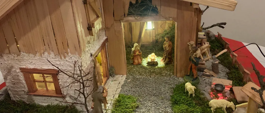 Eine kleine hölzerne Krippe mit Figuren von Jesus, Maria und Josef in einer Stallung. Um die Krippe herum befinden sich kleine Figuren von Tieren und einem Hirten.