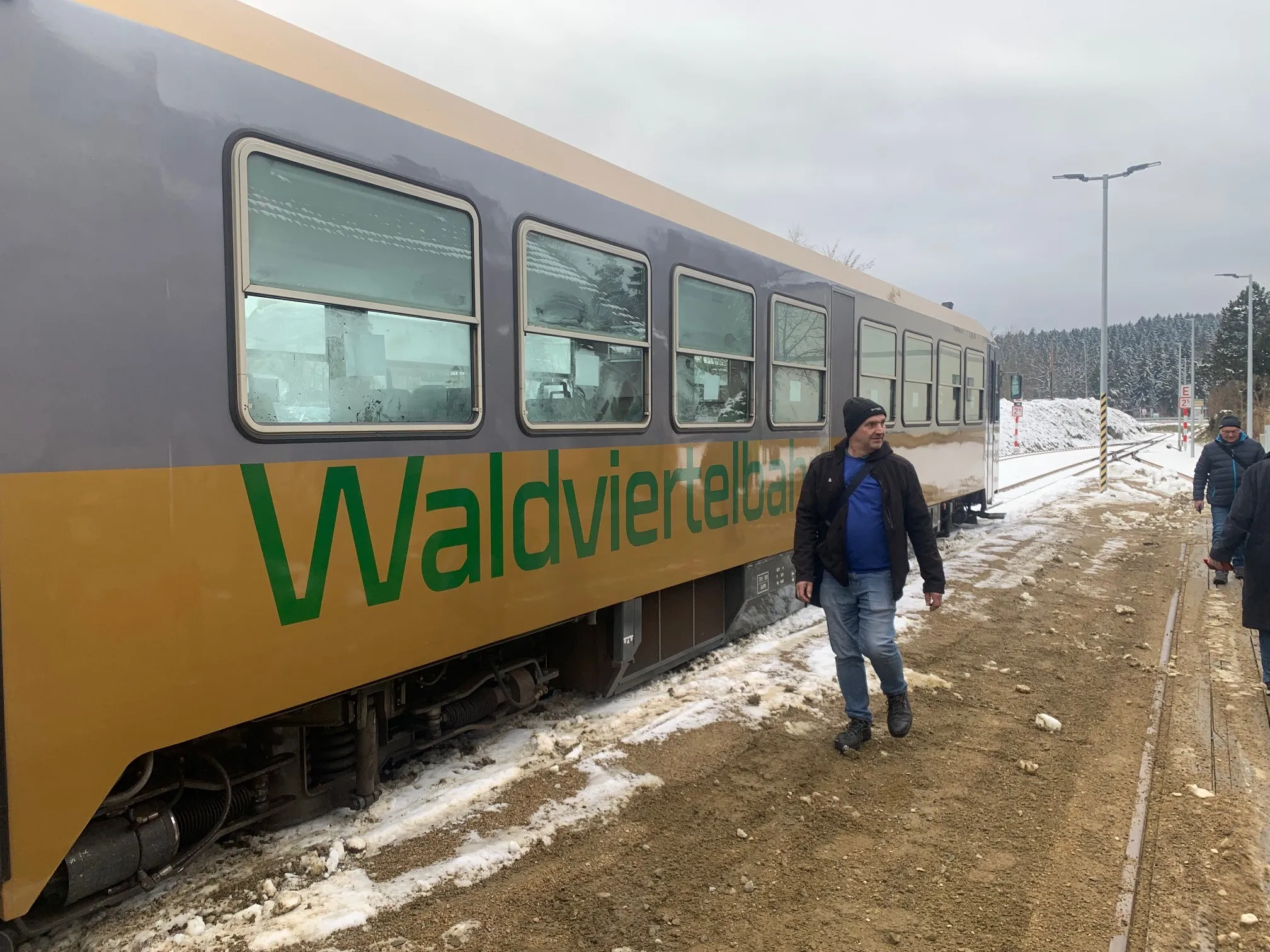 Ein Mann geht an einem Waldviertlerbahn-Zug vorbei, der auf schneebedecktem Boden und mit schneebedecktem Hintergrund steht.