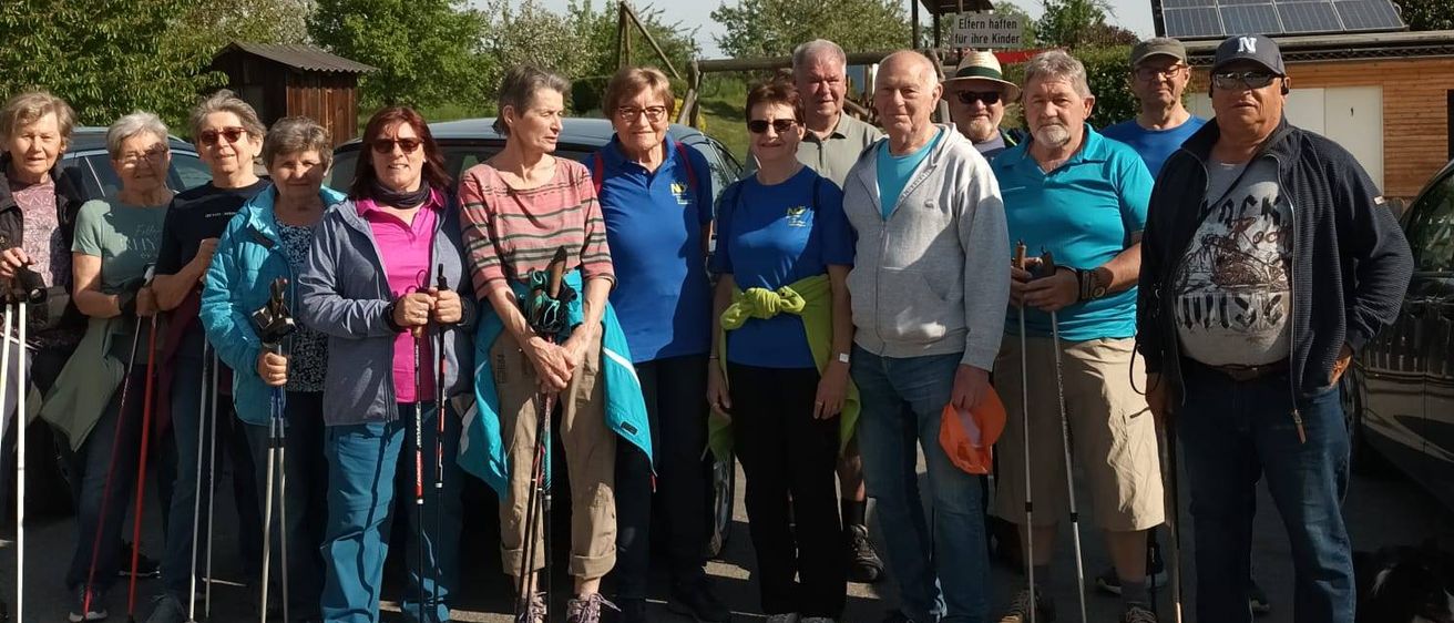 Eine Gruppe von Menschen posiert für ein Foto, trägt Freizeitkleidung und hält Wanderstöcke. Sie stehen vor einem Gebäude mit Solarpanelen.