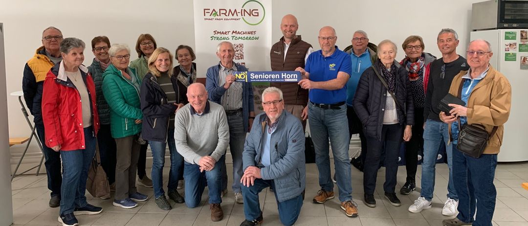 Eine Gruppe Erwachsener in einem Raum, zwei Männer knien und halten ein Schild mit der Aufschrift No Senioren Horn.