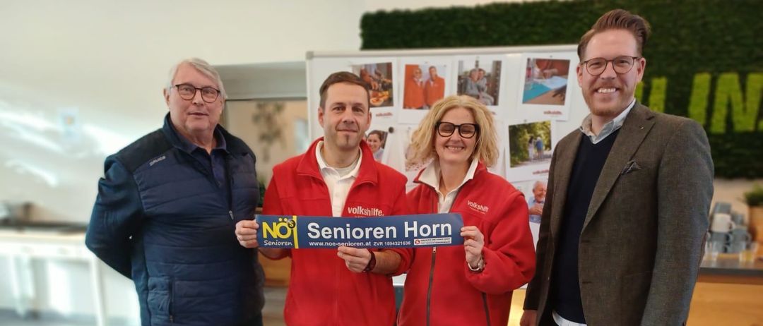 Vier Personen stehen zusammen und halten ein blaues Schild mit der Aufschrift 'NO Senioren Horn'. Sie alle lächeln und scheinen für ein Foto zu posieren.