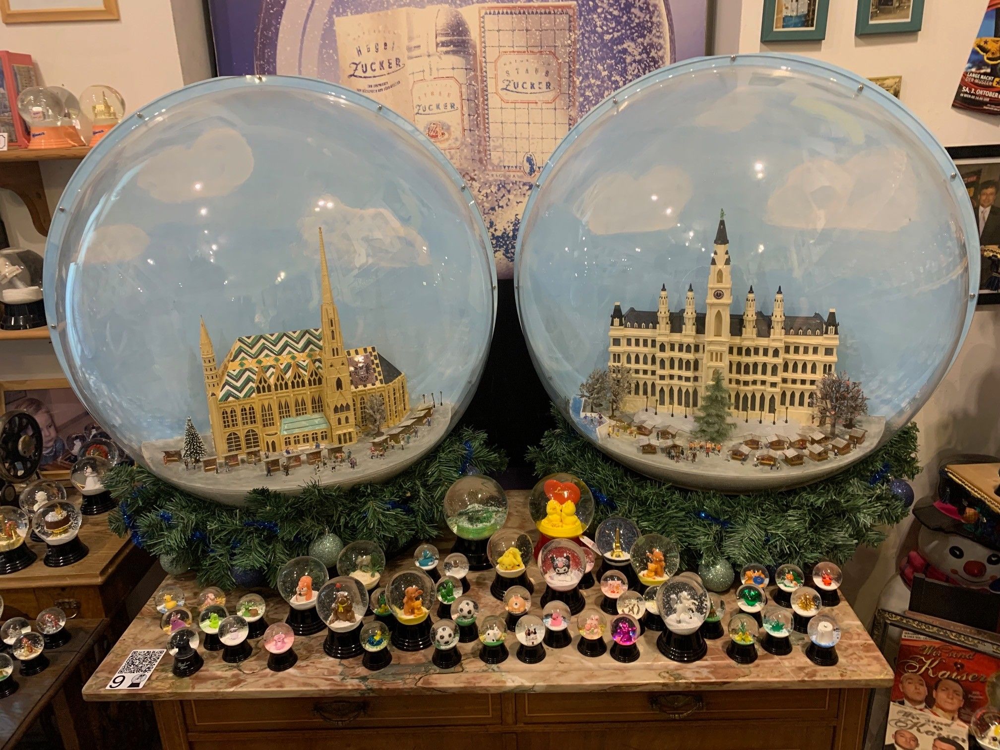 Zwei große Schneekugeln mit detaillierten Miniaturgebäuden im Inneren, eine zeigt eine Kirche und die andere ein Schloss, umgeben von kleineren Schneekugeln mit verschiedenen Charakteren und Objekten.