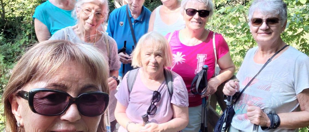 Eine Gruppe älterer Frauen im Wald, lächelnd und posierend für ein Foto. Sie tragen Sonnenbrillen und tragen Wanderstöcke.