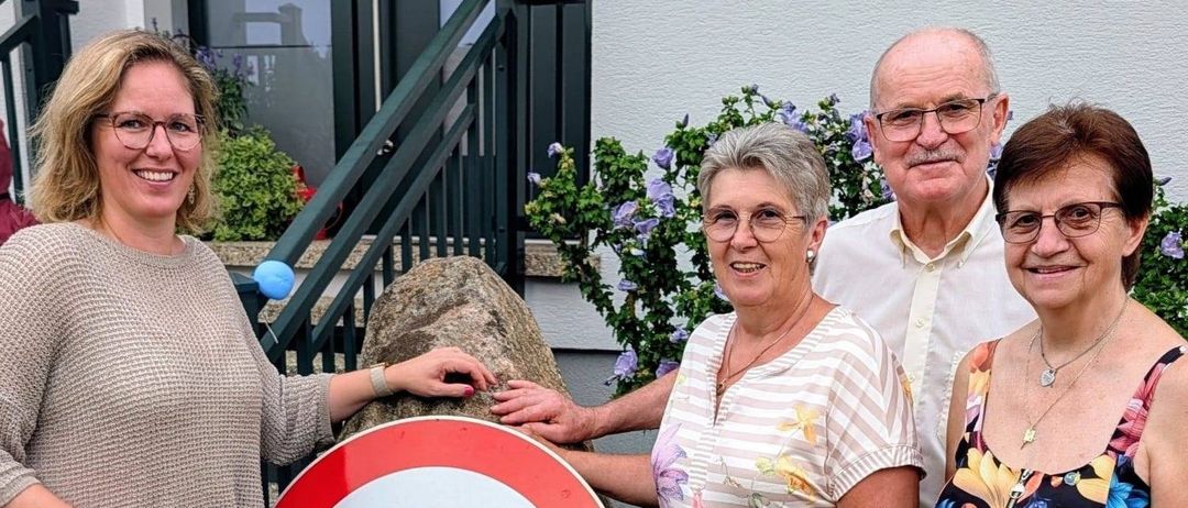 Vier Personen stehen um einen großen Felsen mit einem Geschwindigkeitsbegrenzungsschild darauf. Das Schild zeigt 70. Sie alle lächeln.