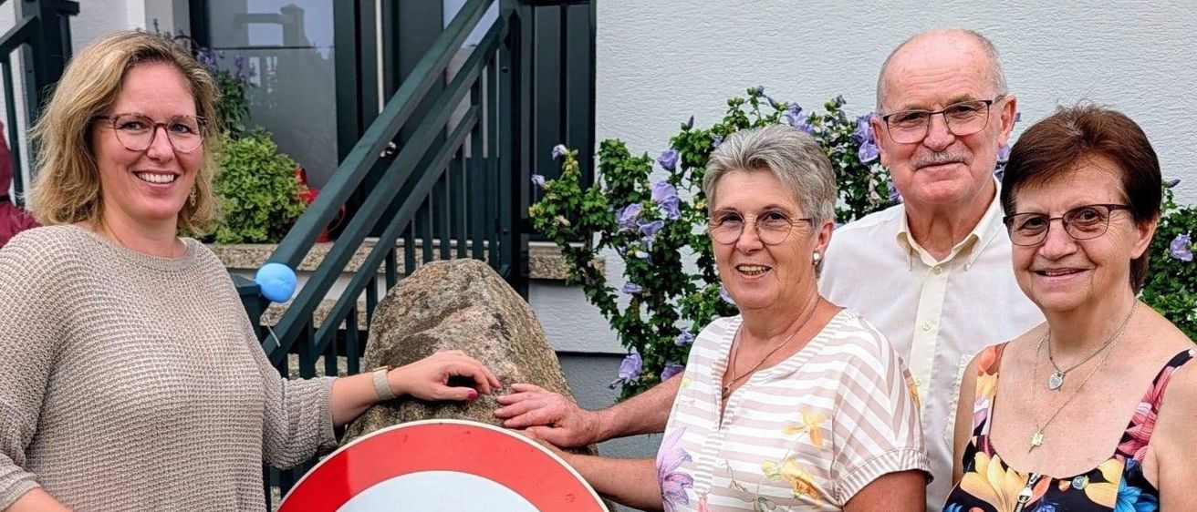 Vier Personen stehen um einen großen Felsen mit einem Geschwindigkeitsbegrenzungsschild darauf. Das Schild zeigt 70. Sie alle lächeln.