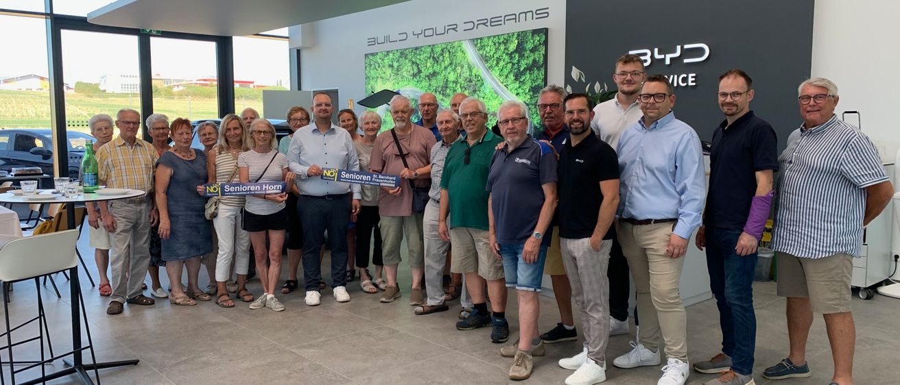 Eine Gruppe von Menschen steht in einem Raum und hält ein blaues Banner mit der Aufschrift NO Senioren Horn. Sie alle lächeln und posieren für ein Foto.