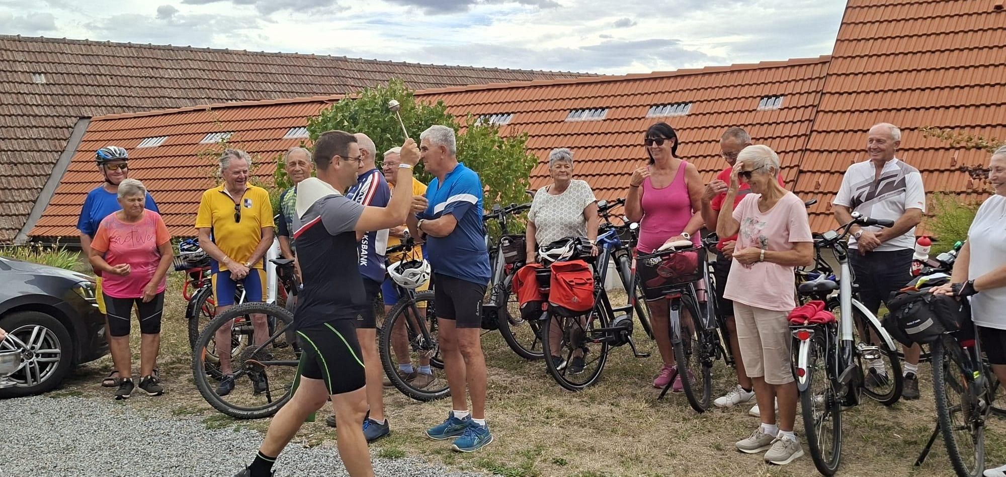 Eine Gruppe älterer Erwachsener steht neben Fahrrädern im Freien, ein Mann hebt einen Golfschläger hoch.