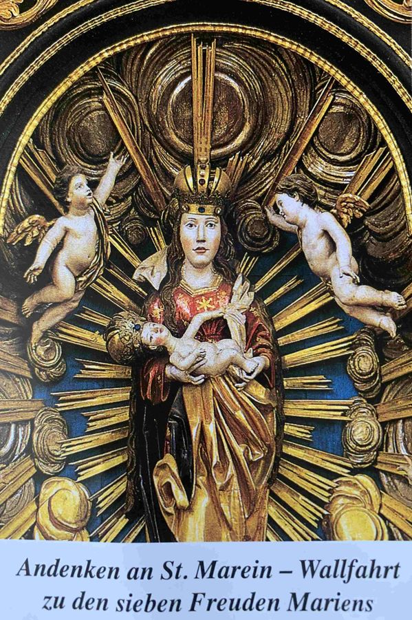 Eine goldene Statue der Jungfrau Maria, die das Jesuskind hält, umgeben von zwei Cherubinen und einem strahlenden Sonnenstrahl.