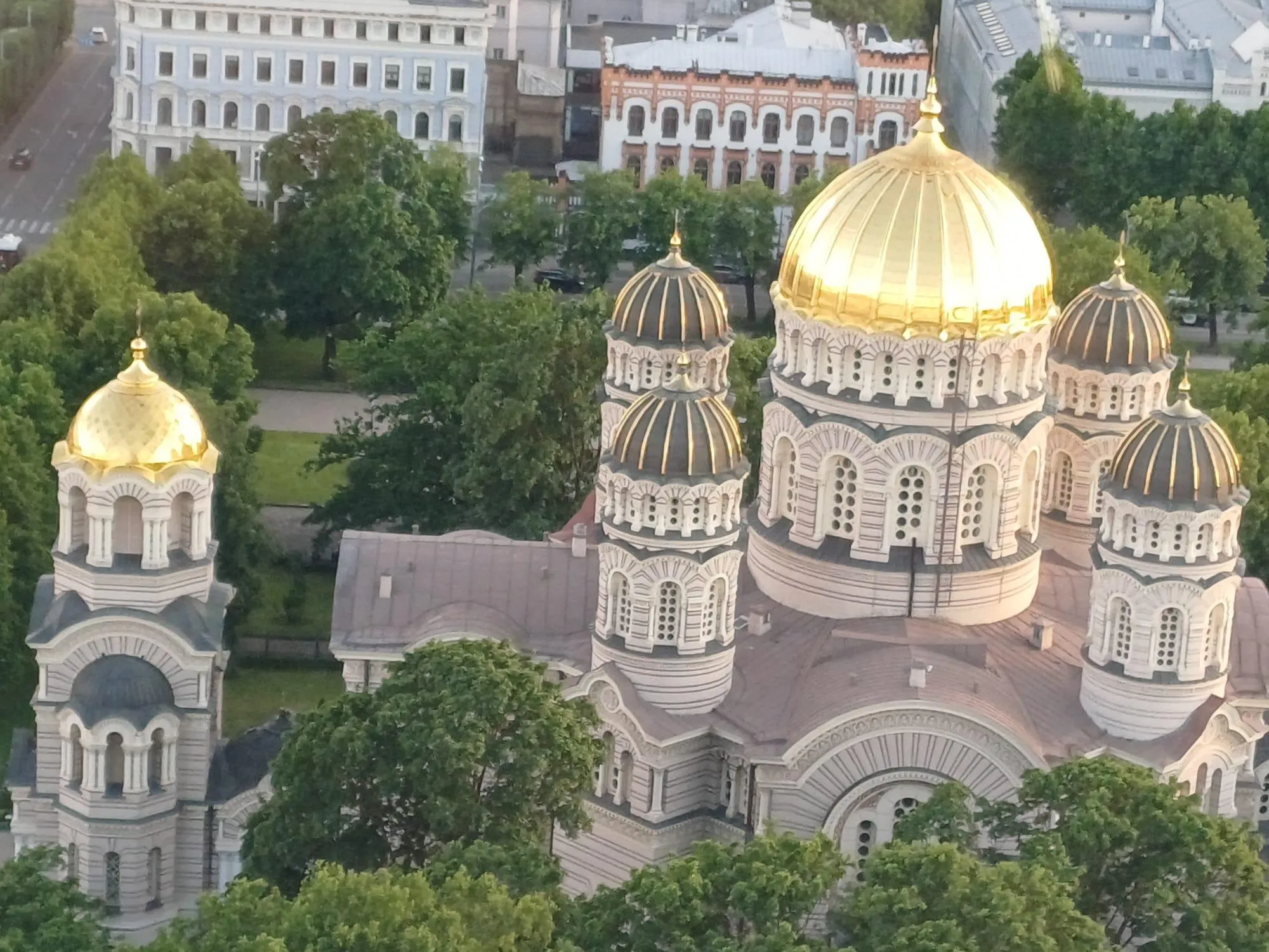 Eine Vogelperspektive einer goldenen Kuppelkathedrale mit filigranen Mustern, umgeben von üppigem Grün und Gebäuden.
