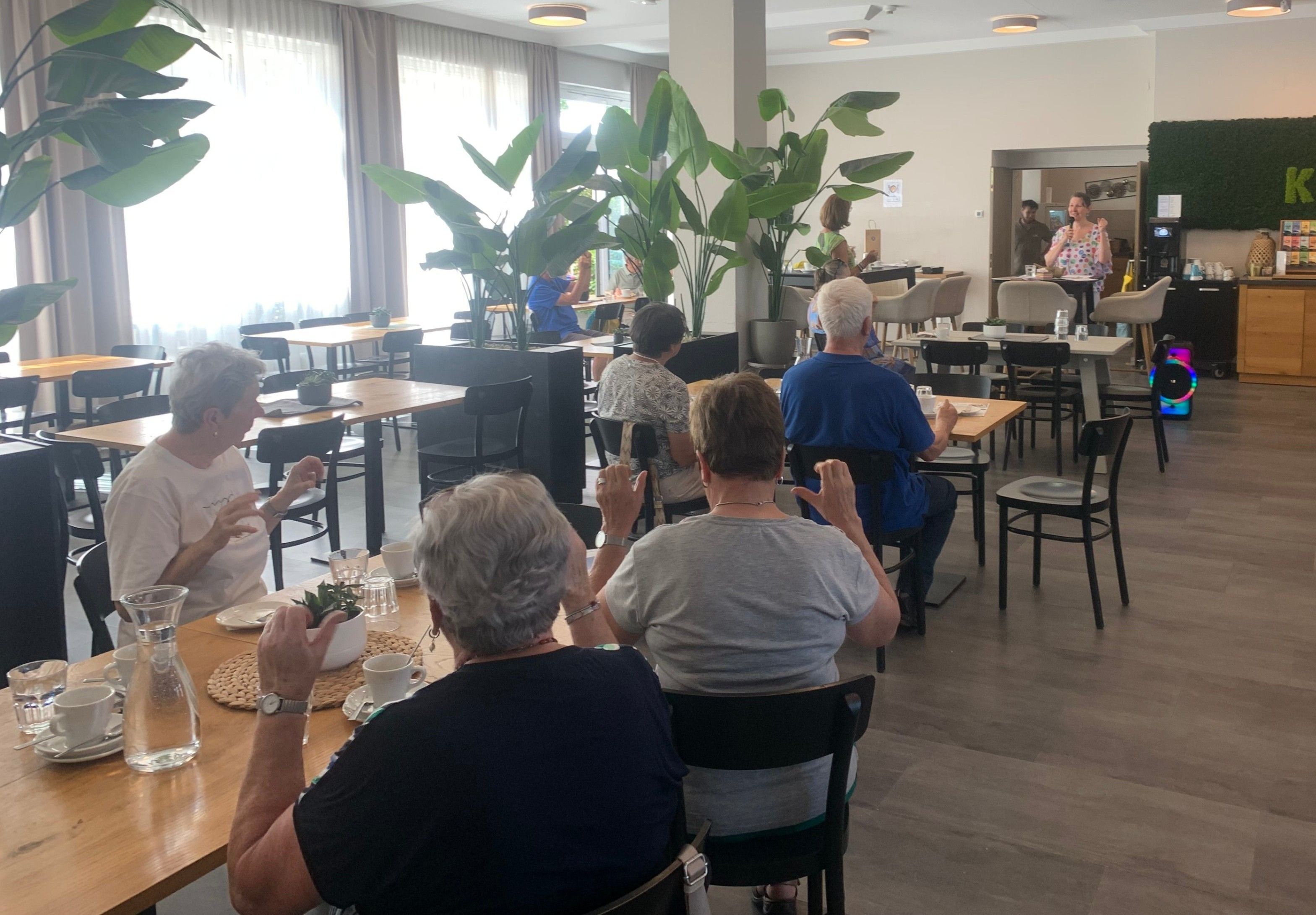 Eine Gruppe älterer Menschen sitzt an einem Tisch in einem Restaurant, möglicherweise im Gespräch. Ein großer Topf steht zwischen ihnen.