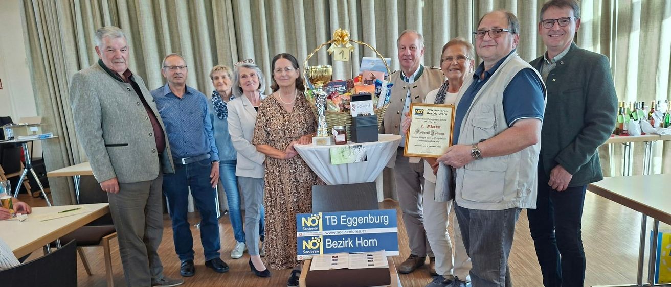 Eine Gruppe von Menschen steht in einem Raum, einige lächeln und eine Person hält eine Trophäe.