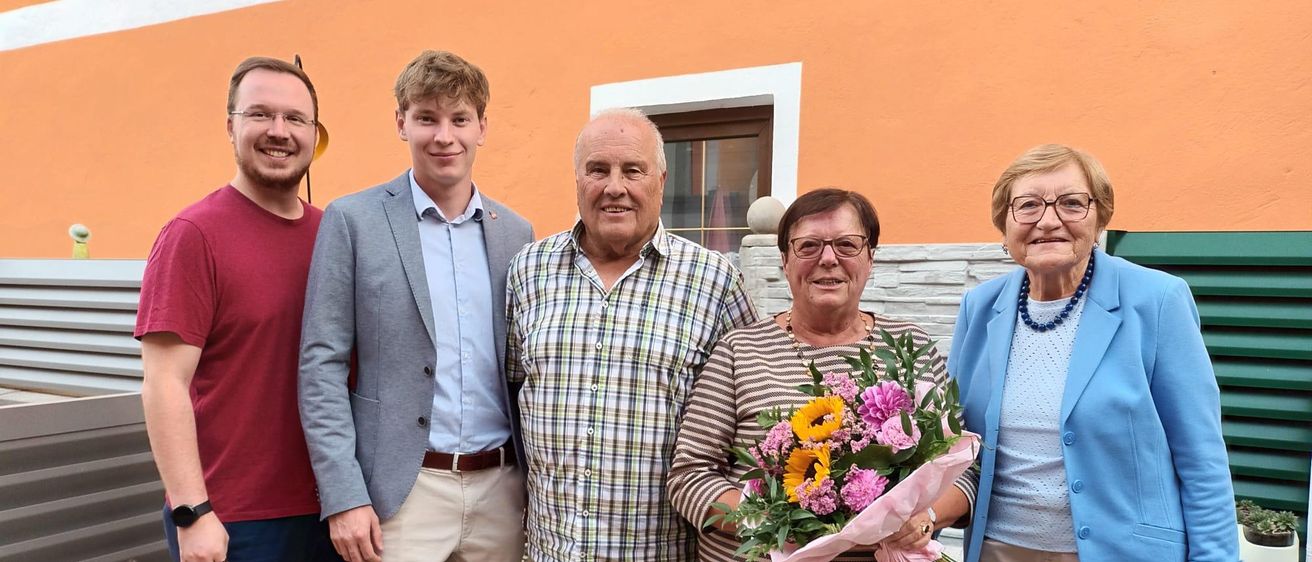 Fünf Menschen stehen vor einem Gebäude. Eine Frau hält einen Blumenstrauß.