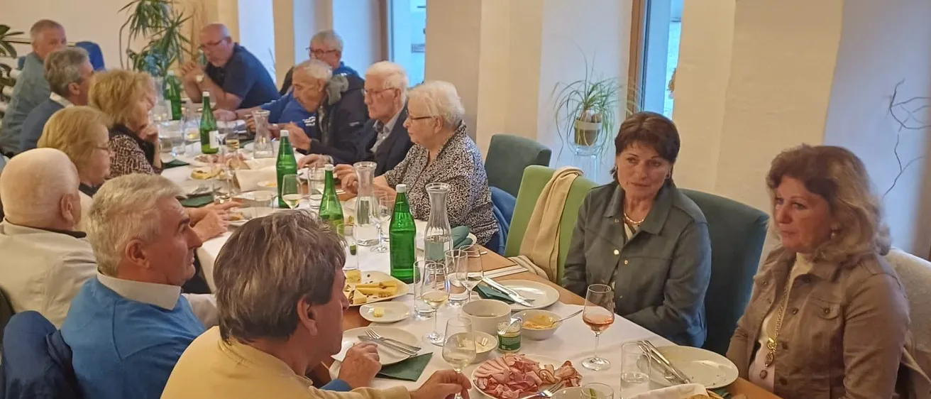 Eine Gruppe älterer Menschen sitzt um einen langen Tisch in einem Esszimmer und isst.