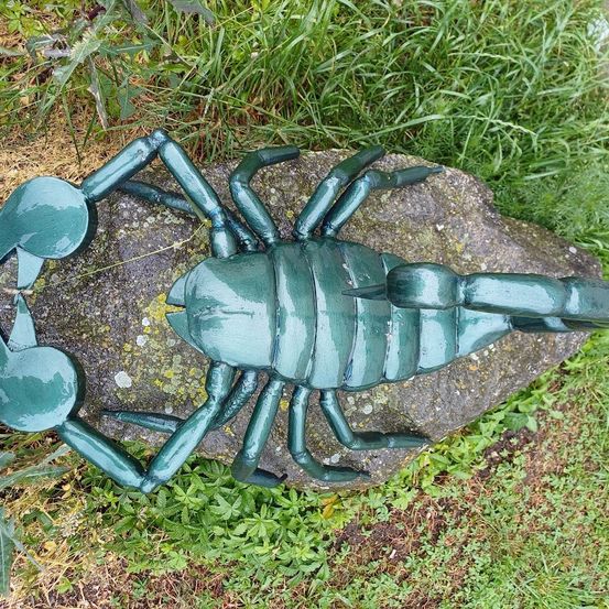 Eine grüne Skorpionskulptur ruht auf einem Felsen mit Gras an einem sonnigen Tag.