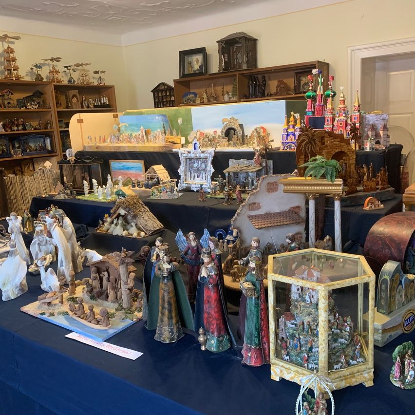 Ein Raum voller verschiedener Figuren und Skulpturen, einschließlich einer Krippe, auf einem Tisch und Regalen. Es gibt auch Bilderrahmen und Schachteln mit Weihnachtsdekoration.