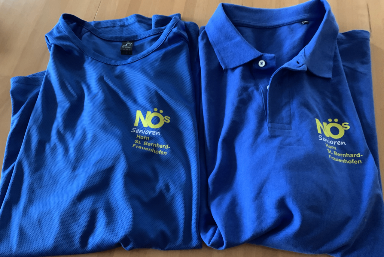 Zwei blaue Poloshirts mit dem Logo NOs Senioren Hom St. Bernhard-Frauenhofen liegen flach auf einer Holzoberfläche.