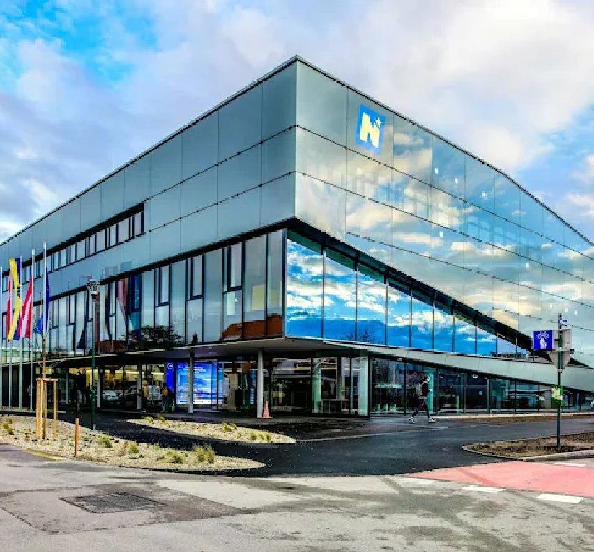 Ein modernes Bürogebäude mit einer großen Glasfassade, einem großen Buchstaben N und einem blauen Himmel mit Wolken.
