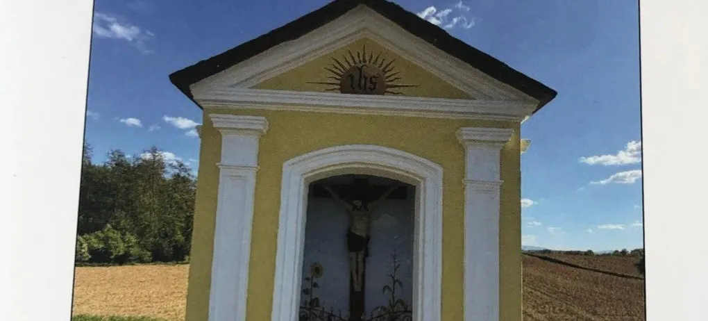 Eine gelbe Kapelle mit einem Kreuz auf der Spitze und dem Bildnis Jesu Christi im Inneren. Die Kapelle ist von Gras und Bäumen umgeben. Das Datum und die Uhrzeit der Veranstaltung sind der 25. Mai 2026 um 18:00 Uhr.