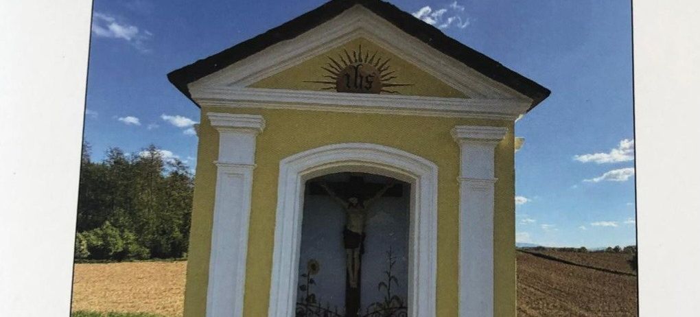 Eine gelbe Kapelle mit einem Kreuz auf der Spitze und dem Bildnis Jesu Christi im Inneren. Die Kapelle ist von Gras und Bäumen umgeben. Das Datum und die Uhrzeit der Veranstaltung sind der 25. Mai 2026 um 18:00 Uhr.