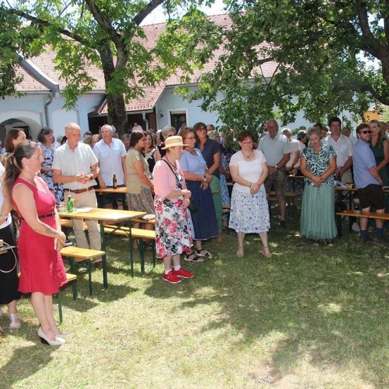 Eine Gruppe von Menschen, möglicherweise eine Familie, versammelt sich in einem Park für eine Veranstaltung im Freien, steht unter einem Baum in der Nähe von Bänken und Tischen.