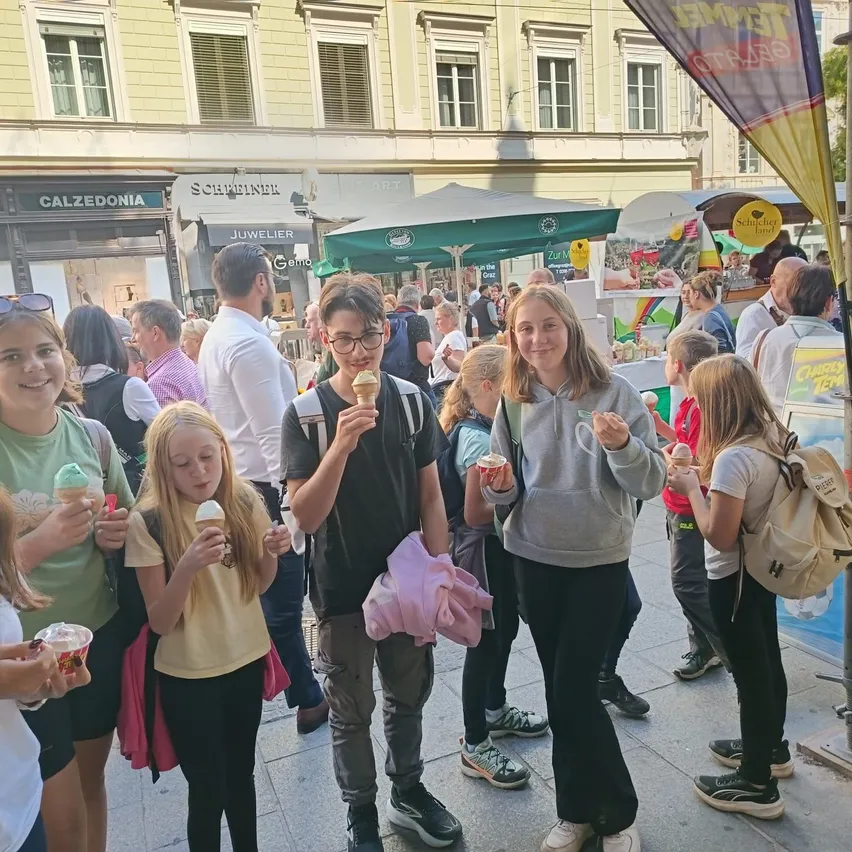 Eine Gruppe von Kindern und Erwachsenen steht vor einem Essensstand und hält Eisbecher in der Hand.