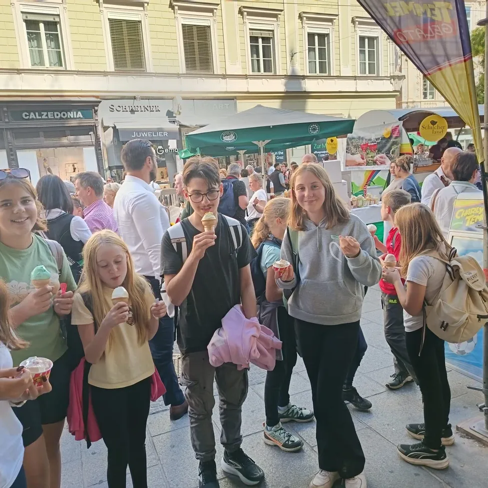 Eine Gruppe von Kindern und Erwachsenen steht vor einem Essensstand und hält Eisbecher in der Hand.