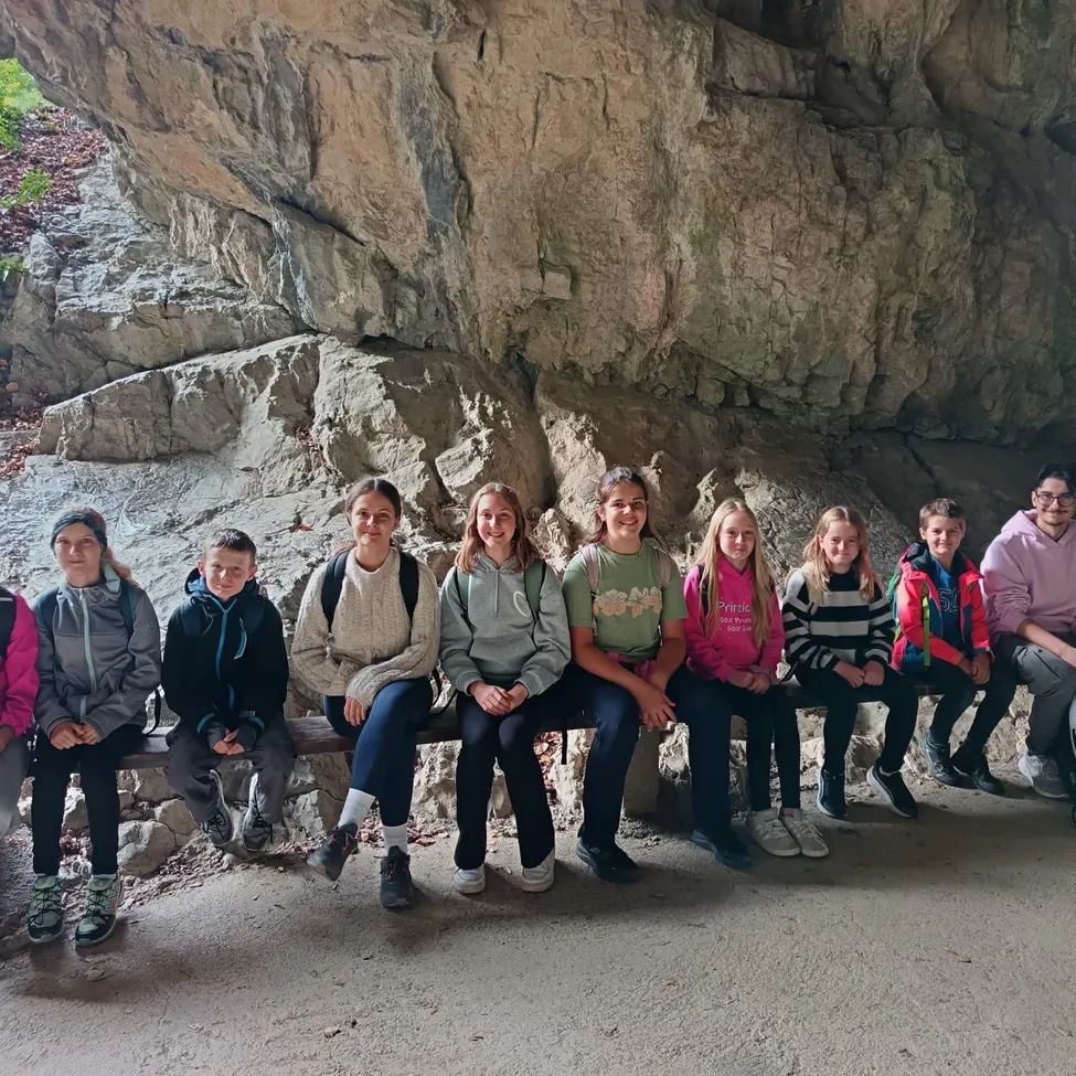 Eine Gruppe von Kindern sitzt auf einer Bank vor einer großen Felsformation.