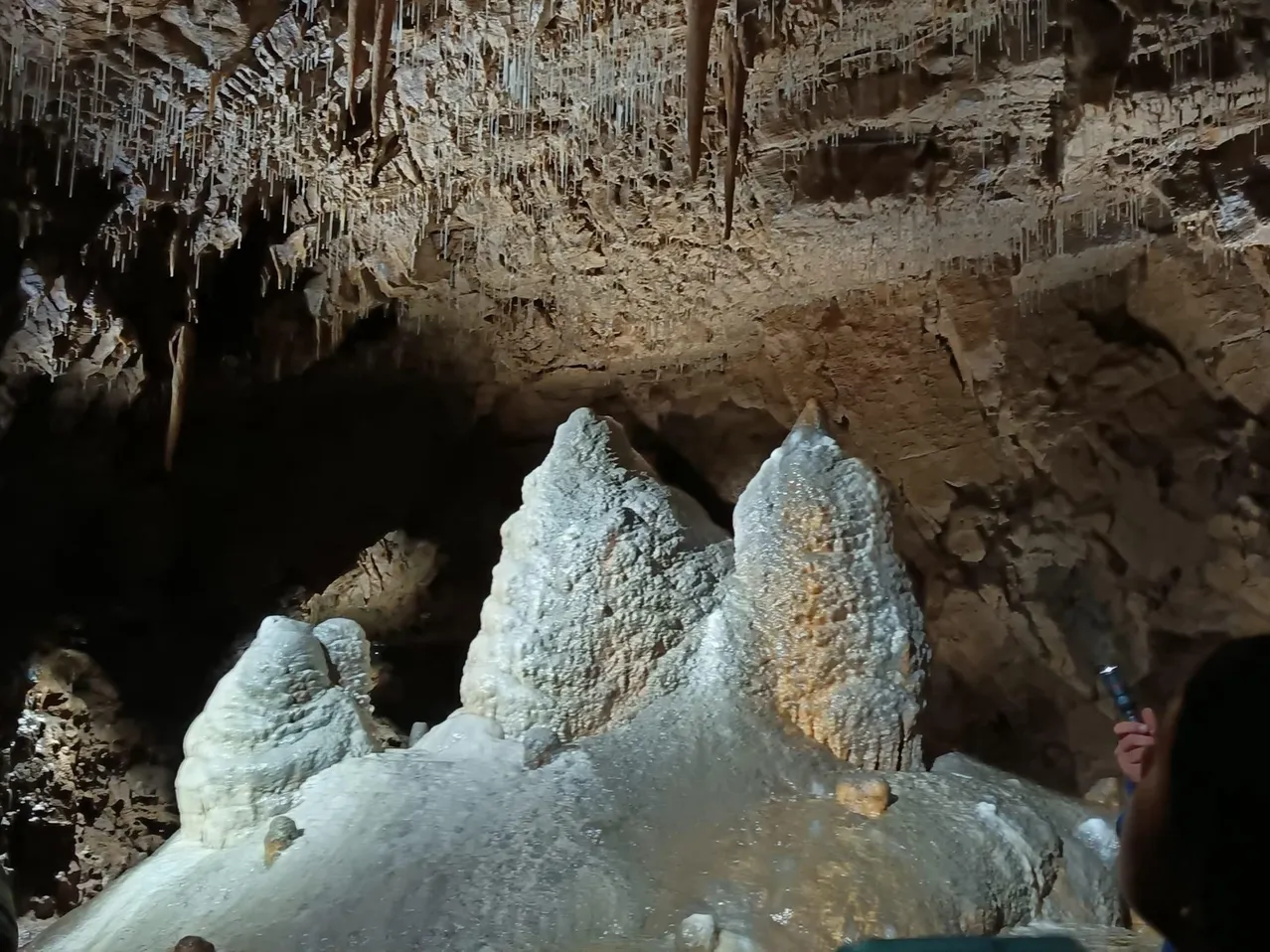 Eine Person fotografiert eine große weiße Felsformation in einer Höhle. Die Felsformation hat eine einzigartige Form und wird von einer Taschenlampe beleuchtet.