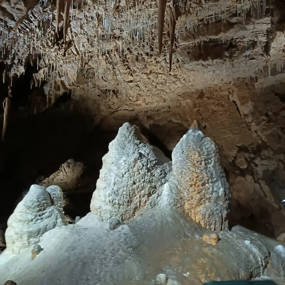 Eine Person fotografiert eine große weiße Felsformation in einer Höhle. Die Felsformation hat eine einzigartige Form und wird von einer Taschenlampe beleuchtet.