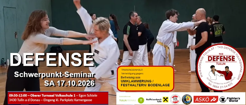 Eine Gruppe von Menschen praktiziert Kampfsport in einer Turnhalle. Zwei Frauen sind im Vordergrund, eine trägt eine Brille und die andere ein weißes Uniform, beide führen eine Kampfsportbewegung aus. Im Hintergrund praktiziert ein Mann in einem schwarzen Shirt ebenfalls Kampfsport.