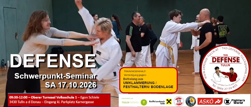 Eine Gruppe von Menschen praktiziert Kampfsport in einer Turnhalle. Zwei Frauen sind im Vordergrund, eine trägt eine Brille und die andere ein weißes Uniform, beide führen eine Kampfsportbewegung aus. Im Hintergrund praktiziert ein Mann in einem schwarzen Shirt ebenfalls Kampfsport.