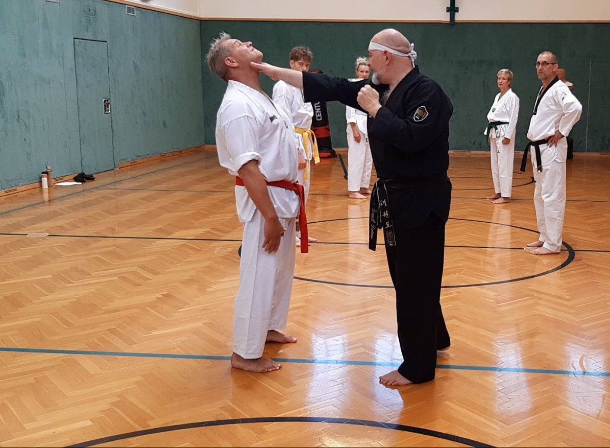 Ein Kampfsportlehrer korrigiert die Haltung eines Schülers während eines Kurses in einer Turnhalle.