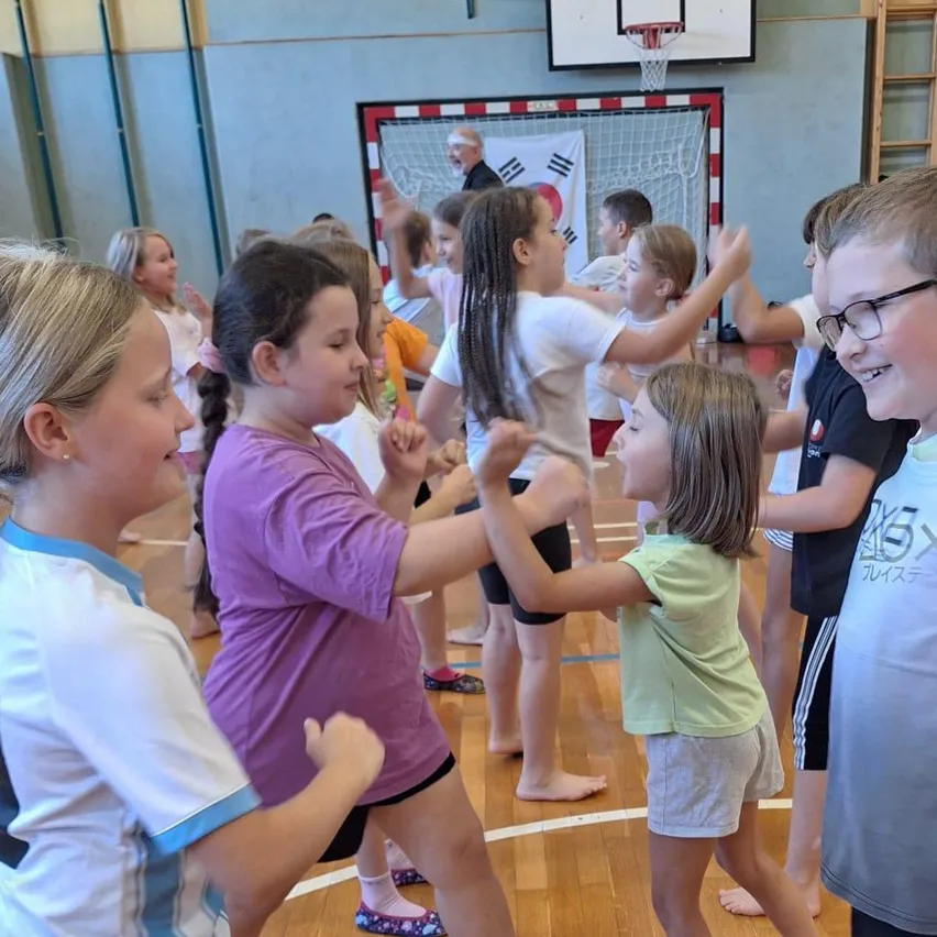 Eine Gruppe von Kindern spielt ein Spiel in einer Turnhalle. Sie alle lächeln und scheinen Spaß zu haben.