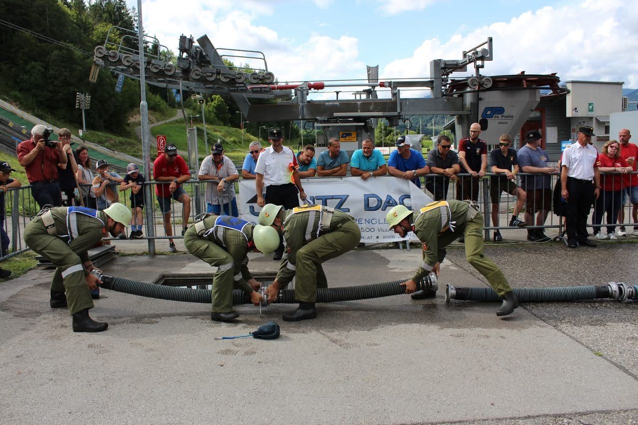 Eine Gruppe von Männern in grünen Uniformen arbeitet an einer Pipeline, während Zuschauer hinter einem Zaun zusehen.