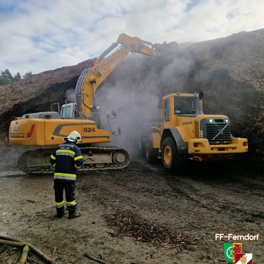 A firefighter oversees two yellow machinery vehicles on a dirt road. The vehicle on the left is an excavator, while the one on the right is a bulldozer.
